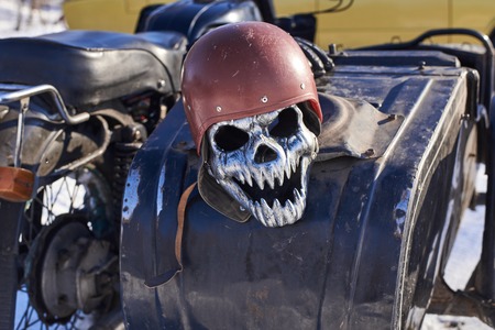Iron mask in the form of a skull in a old helmet lying on a motorcycleの写真素材