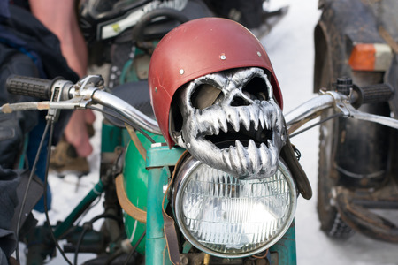 Iron mask in the form of a skull in a old helmet lying on a headlight of motorcycleの写真素材