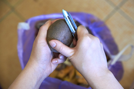 Women's hands peeling potatoes with a special knife, home cookingの写真素材