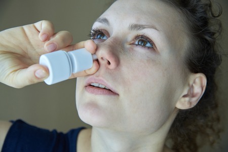 Girl sprays the spray from runny nose into the nasal passの写真素材