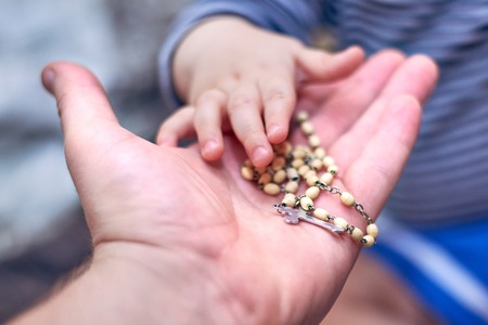 A small child takes a rosary from his dad's hand