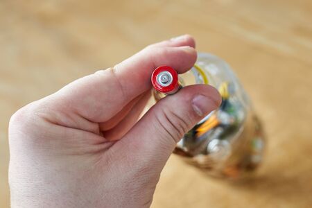 A man holds used batteries to throw in a plastic bottle, on a wooden background, the topic of...