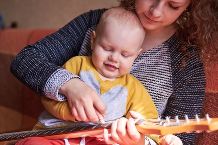 Mom teaches her little cute son to play the guitar. Early child development.