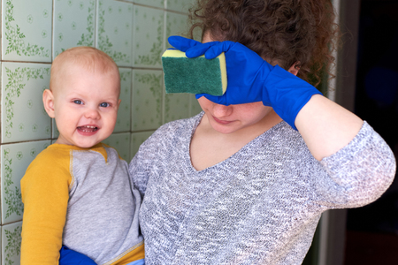 A tired mother with her little son is cleaning the house. The concept of combining homework and raising a child.の写真素材