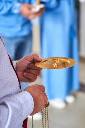 A priest holds a gold plate with wedding rings at a wedding ceremony in a Christian church.の写真素材
