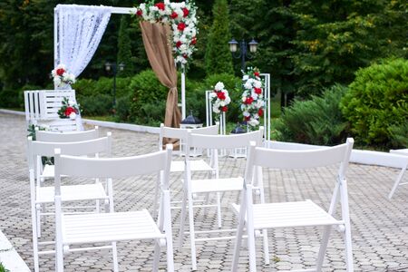 Beautiful outdoor wedding decorations, arch decorated with red and white flowers, chairs, lanterns.の写真素材
