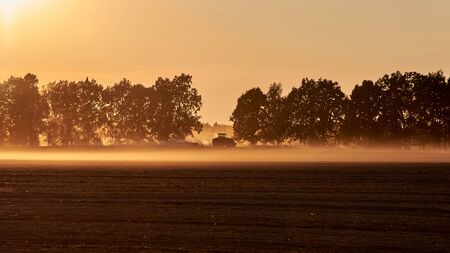 Silhouette of a tractor that harvests in the field in autumn, beautiful panorama