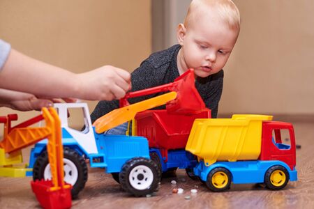 Mom shows her little son how to play with a toy tractor and dump truck.の写真素材