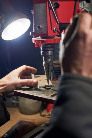 Hands of a man who drills a metal part on a machine tool in a home workshop.の写真素材