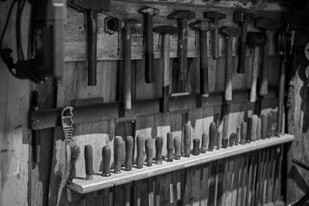Old tools - hammers and files of different sizes on a wooden wall, black and white photo.の写真素材