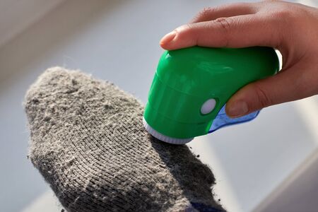 Woman removes lint from wool socks with the help of an electric machine, close-up.の写真素材