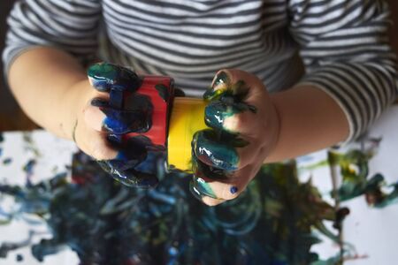 Hands of a child with tubes of paint who paints with bright finger paints, the early development of...