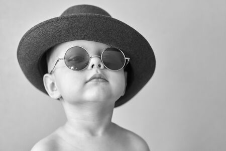 Portrait of a little cute funny boy in a retro hat and round glasses, black and white photo.