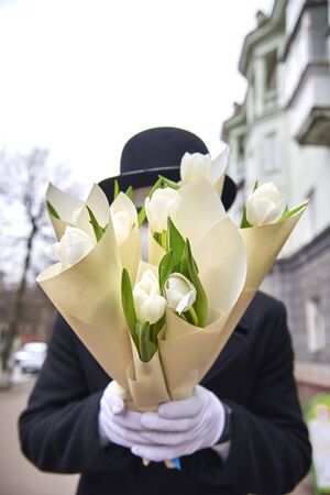 Mime holds white tulips in paper packaging on a city street.