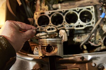 A man holds a piston of a car against the background of an engine, car repair process.の写真素材