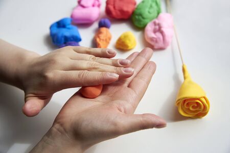 The hand of a girl who sculpts roses from light airy multi-colored plasticine, developing activities.の写真素材