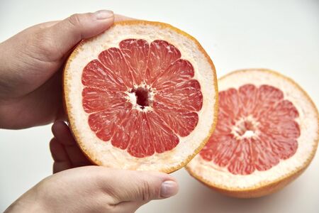 Half of fresh ripe grapefruit in woman's hands on a light background, food concept.の写真素材
