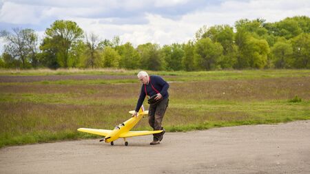 An elderly man launches a radio-controlled aircraft on the runway in the spring.