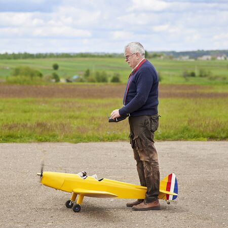 An elderly man launches a radio-controlled aircraft on the runway in the spring.の写真素材