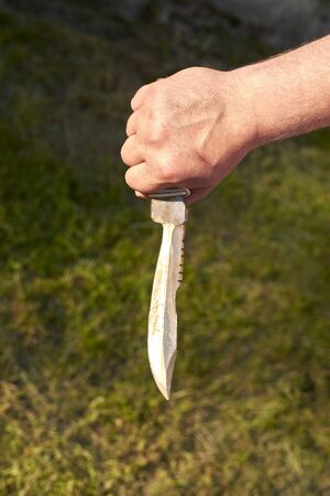 Sharp old notch knife in man's hand on grass background.