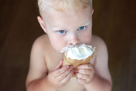 Portrait of a little blue-eyed fair-haired boy eats ice cream.の写真素材