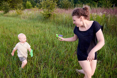 Two year old boy playing with his mom with water pistols in the grass meadow, summer fun.の写真素材