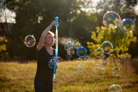 Woman blowing soap bubbles on the meadow in summer, summer fun, summer time, selective focus.