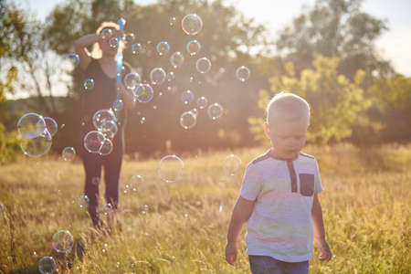 Mom and baby blow soap bubbles on a sunny meadow in summer, summer fun, selective focus.