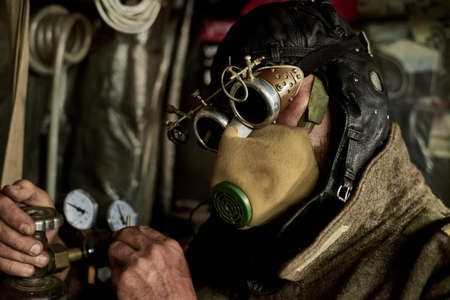 A man in a respirator and glasses in the style of steampunk works with a pressure gauge and a cylinder, postapokalipsis concept.の写真素材