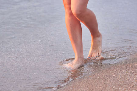 Legs of a woman who walks on the water on the beach at sea at sunrise. Travel Concept.