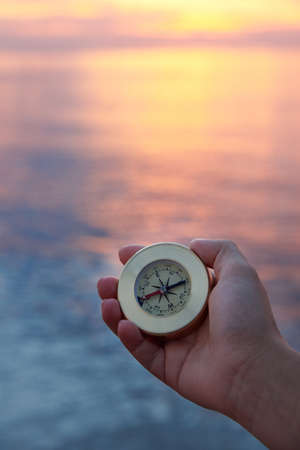 Woman's hand with a compass on the sea coast at sunrise. Travel concept.