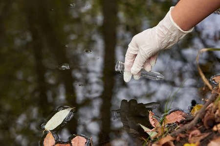 A scientist collects river water in a glass beaker for testing.