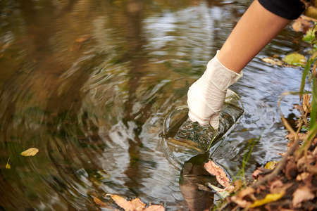 A scientist collects river water in a glass beaker for testing.