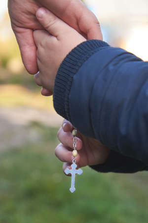 Dad and little son hold each other's hand with a rosary, Christian religion concept.