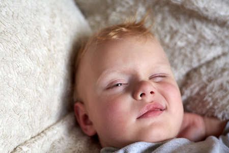 A portrait of a three-year-old blonde funny boy waking up in his bed.