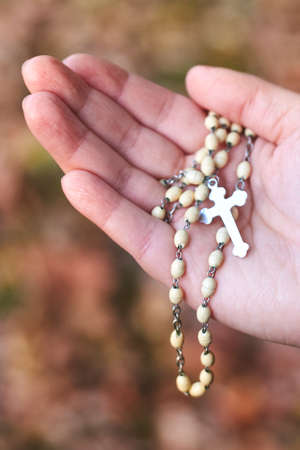 Women's hands holding rosary at the autumn background, close-up.