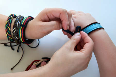 Woman ties a leather bracelet on the arm of a child on a white background, close-up.
