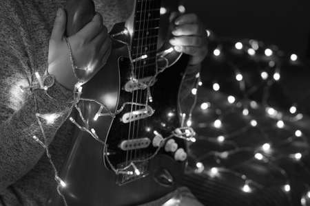 Electric guitar in the hands of a woman against the background of garlands, black and white photo.の写真素材