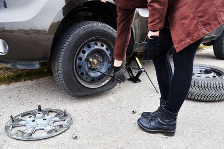 A young woman removes the wheel with a key near her car with a flat tire, trouble on the road.の写真素材
