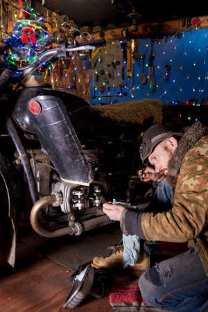 A man repairs an old motorcycle in the garage on New Year's Eve.の写真素材