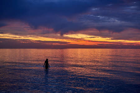Silhouette of a beautiful woman in the water at sea dawn.