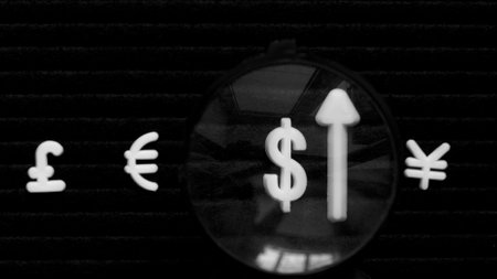 Currency signs, pound, euro, dollar and yen on a black background. The dollar is magnified under a magnifying glass.の写真素材