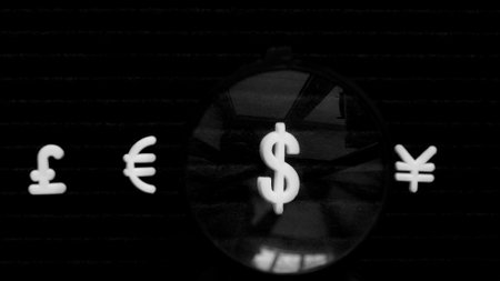 Currency signs, pound, euro, dollar and yen on a black background. The dollar is magnified under a...