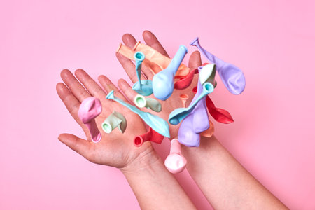 Multicolored not inflated balloons thrown into the air from the hands of a woman on a pink...