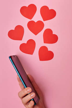 Paper hearts flying out of a smartphone, top view, Valentine's day in the hands of a woman, love and technology concept.の写真素材