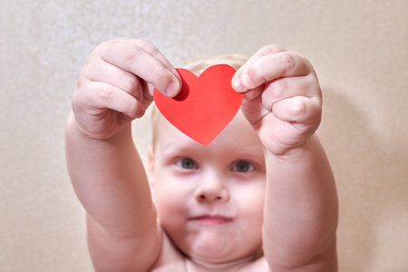Little smiling boy holding a paper red heart, selective focus, the theme of love and hope.の写真素材