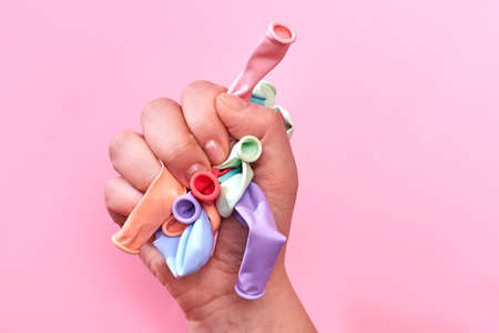 Multicolored not inflated balloons in the hands of a woman on a pink background, creative background.の写真素材