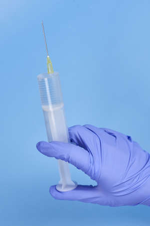 Woman's hands in medical gloves hold a syringe on a blue background, vaccination concept.