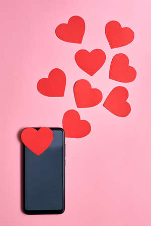 Paper hearts flying out of a smartphone, top view, Valentine's day, love and technology concept.の写真素材