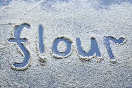 The word flour is written on scattered flour on a blue background, the theme of cooking.の写真素材